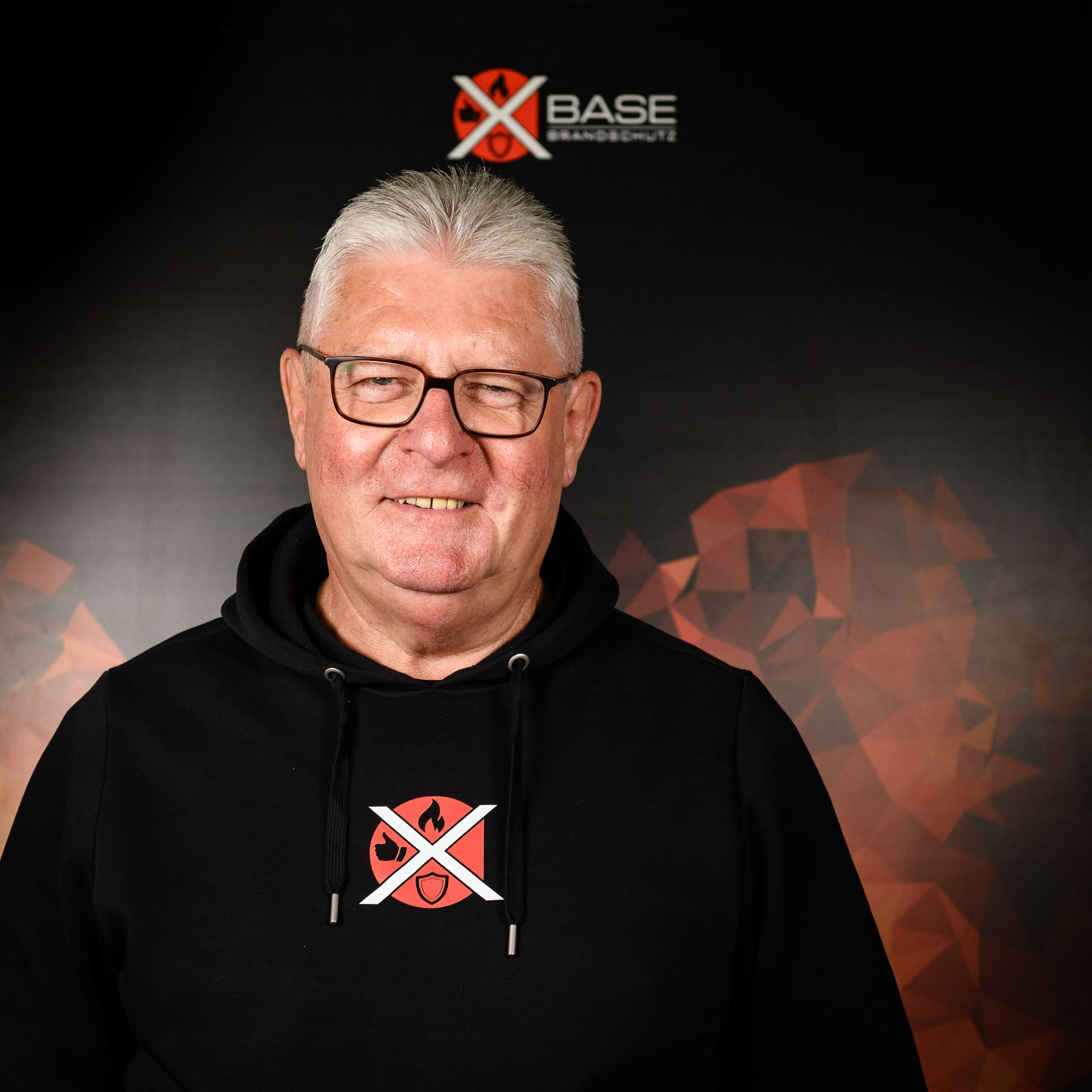 Portraitaufnahme eines Mitarbeiters der Brandschutzfirma x-base vor Flammendesign-Plakat