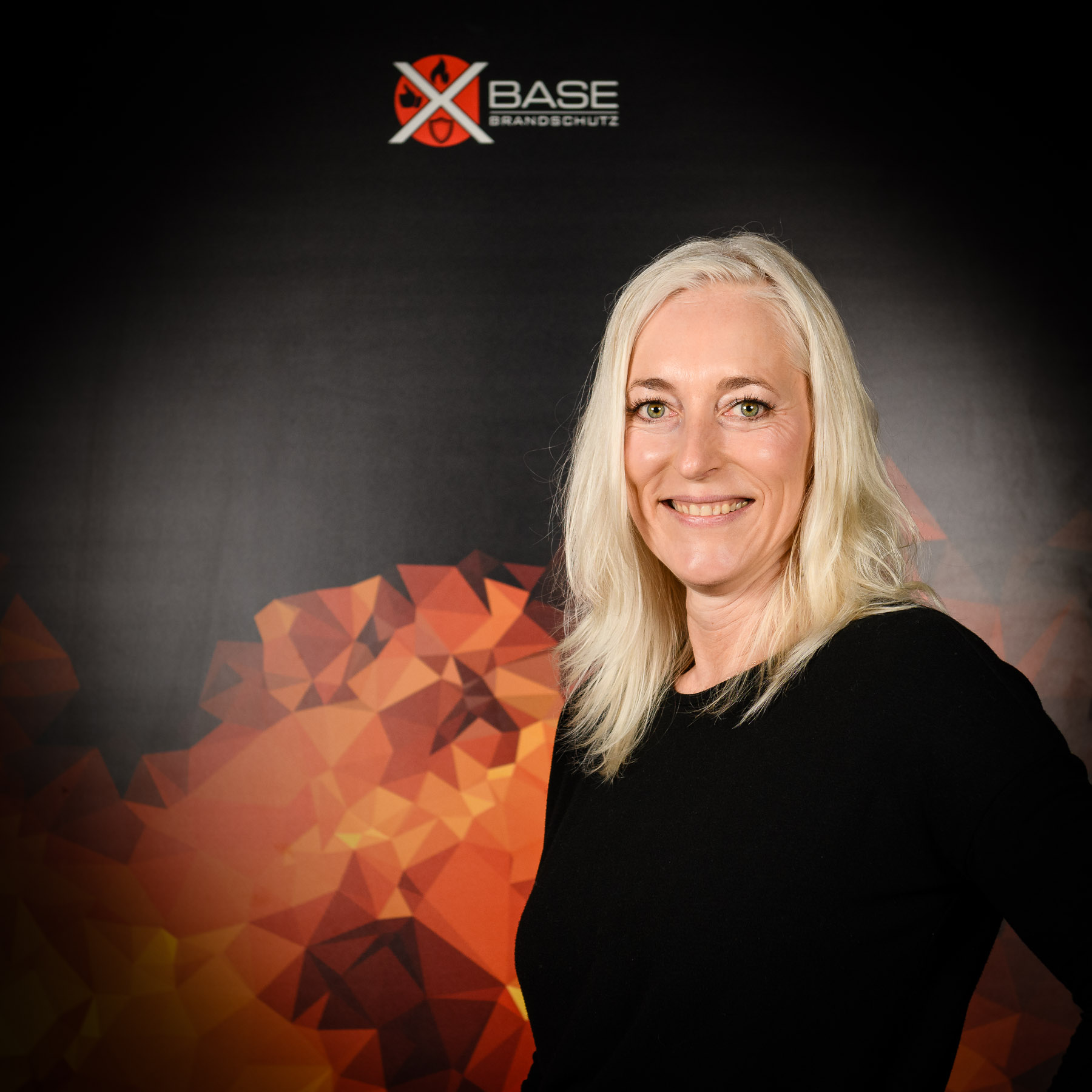 x-base-brandschutz-Mitarbeiter_a-3 Mitarbeiterin der Brandschutzfirma x-base steht vor Flammendesign-Plakat Portraitbild