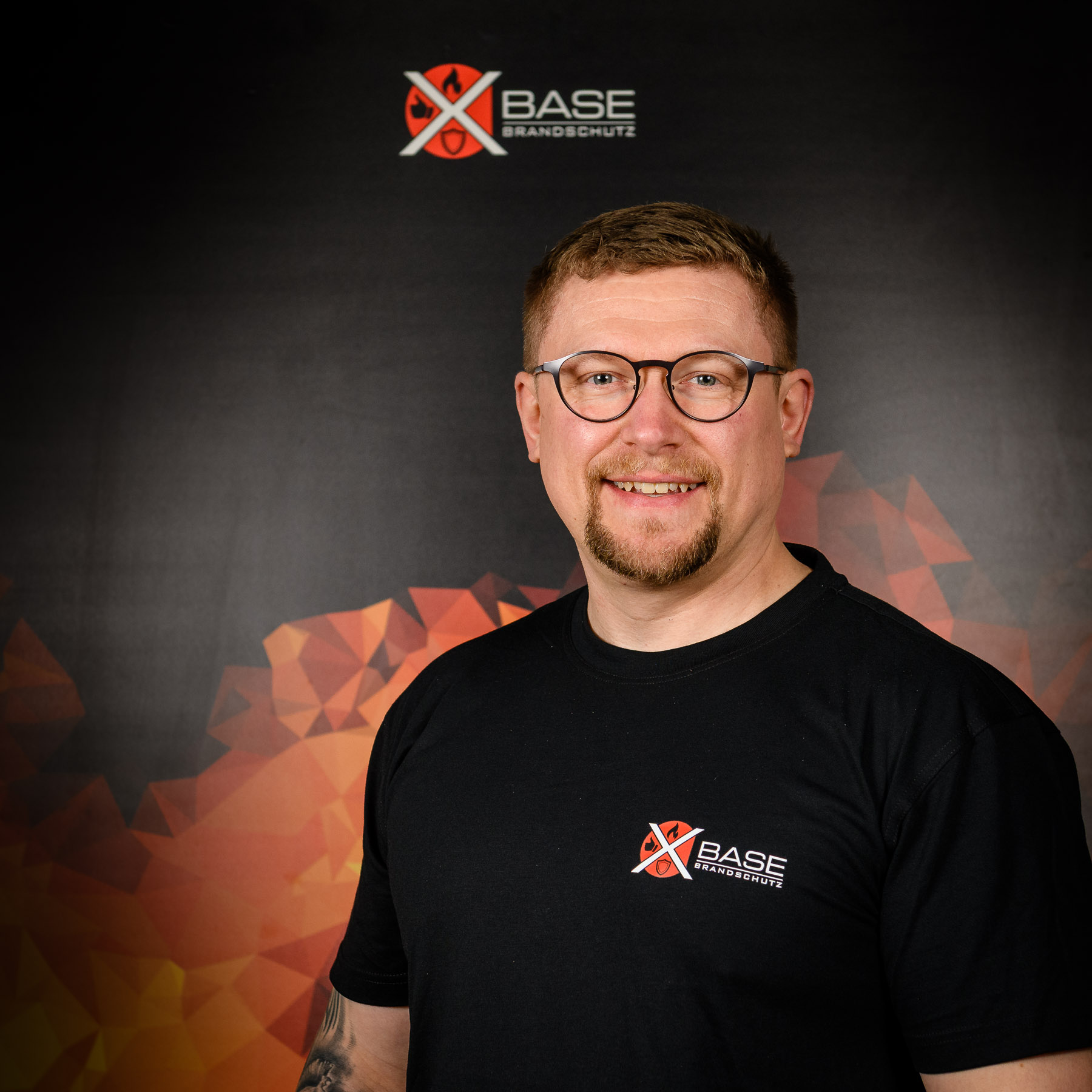 Portraitaufnahme eines Mitarbeiters der Brandschutzfirma x-base vor Flammendesign-Plakat